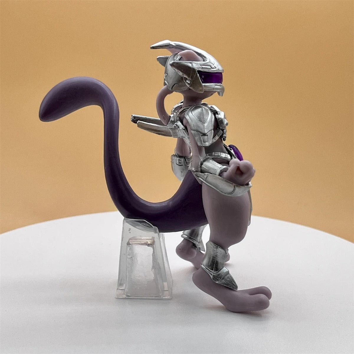 Mechanical cat-like figure with a purple tail on a white platform against a beige background